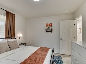 Ein Schlafzimmer mit einem Bett, einem Nachttisch, einer Lampe, einer Tür und einem an der Wand befestigten Regal mit Dekorationen.