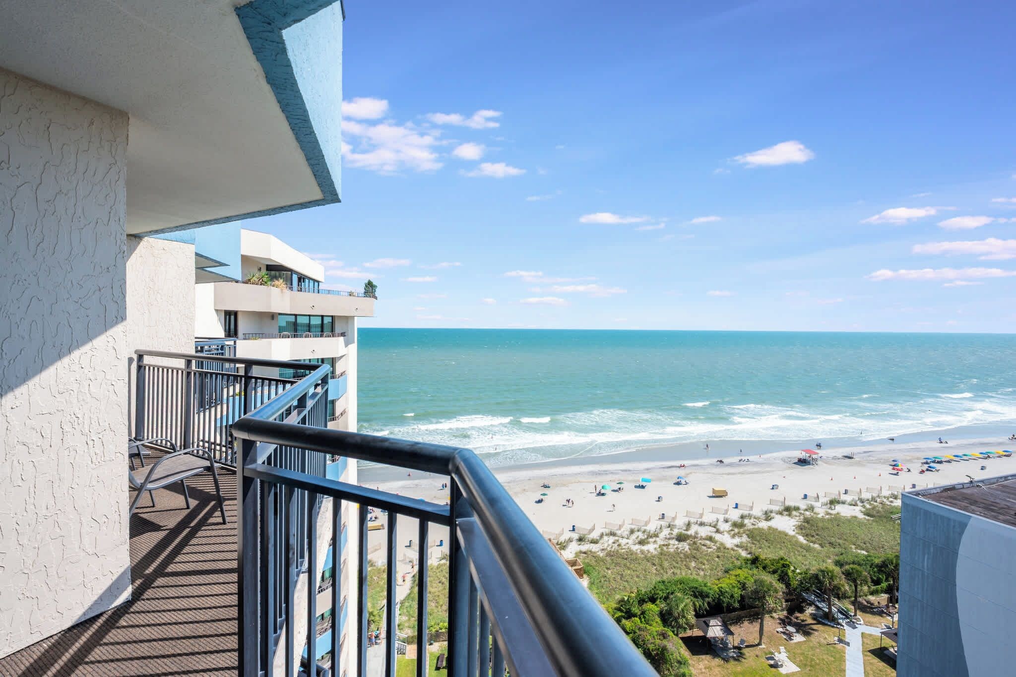 A balcony overlooking a beach with a view of the ocean and a clear sky.