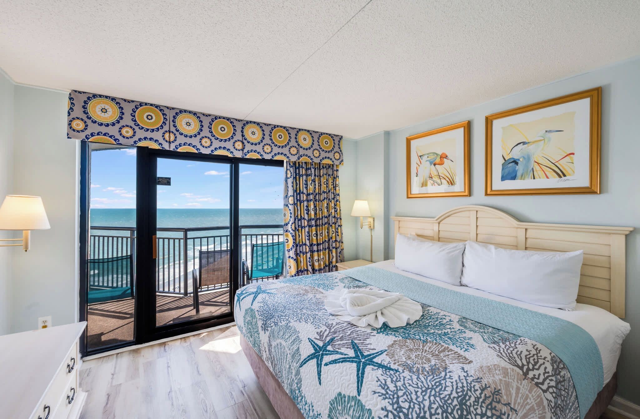 Une chambre d’hôtel avec un lit, une vue sur la mer et deux tableaux accrochés au mur.