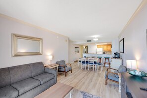 Ein modernes Wohnzimmer mit einem grauen Sofa, einem Holztisch und einem Essbereich mit weißem Tisch und Stühlen.
