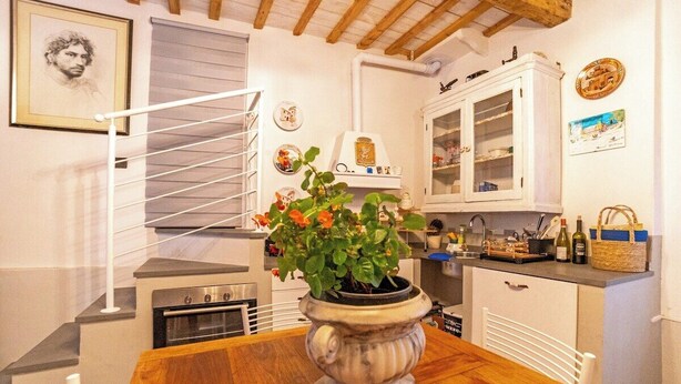 Una cocina con armarios blancos, una escalera de madera y una planta en maceta sobre la mesa.