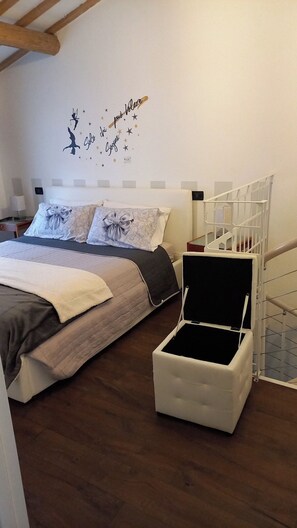 Ein Schlafzimmer mit einem Bett, einer dekorativen Wandverklebung, einer weißen Kommode und einer Holzbalkendecke.