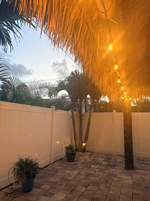 An outdoor patio area with a white fence, potted plants, and string lights. - Beautiful beach home steps from private beach.  Fenced in yard with jacuzzi. (Redington Beach)