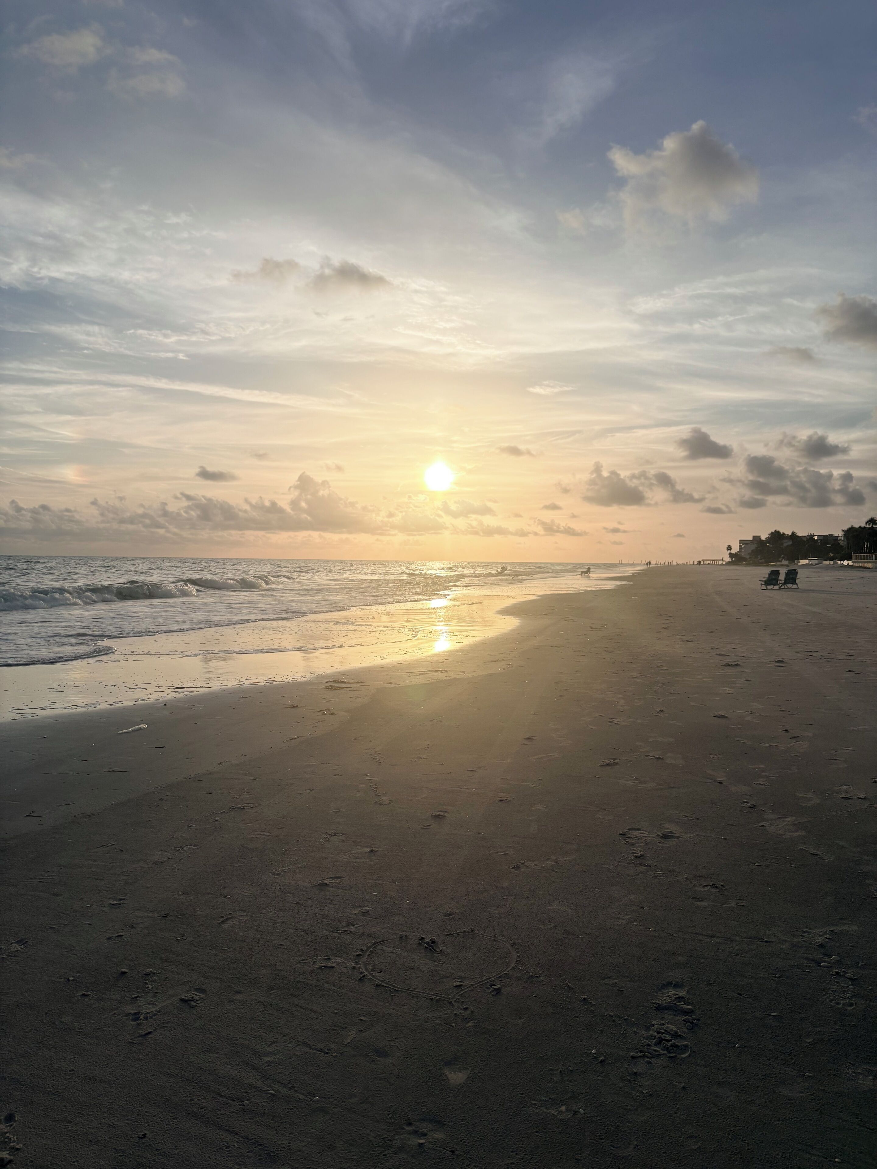 Uma praia com pegadas que levam à água, céu claro e um pôr do sol.