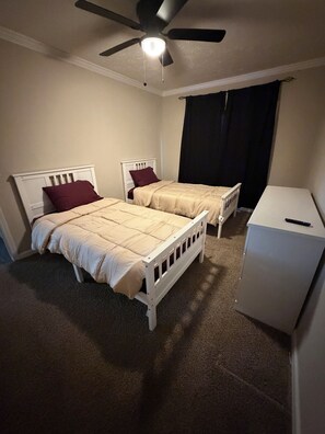 Ein Schlafzimmer mit zwei Einzelbetten, einem Deckenventilator, einem weißen Kleiderschrank und einem dunklen Vorhang.