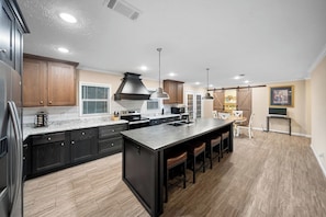 Una cocina moderna con muebles oscuros, una isla grande con taburetes y un comedor con mesa y sillas.