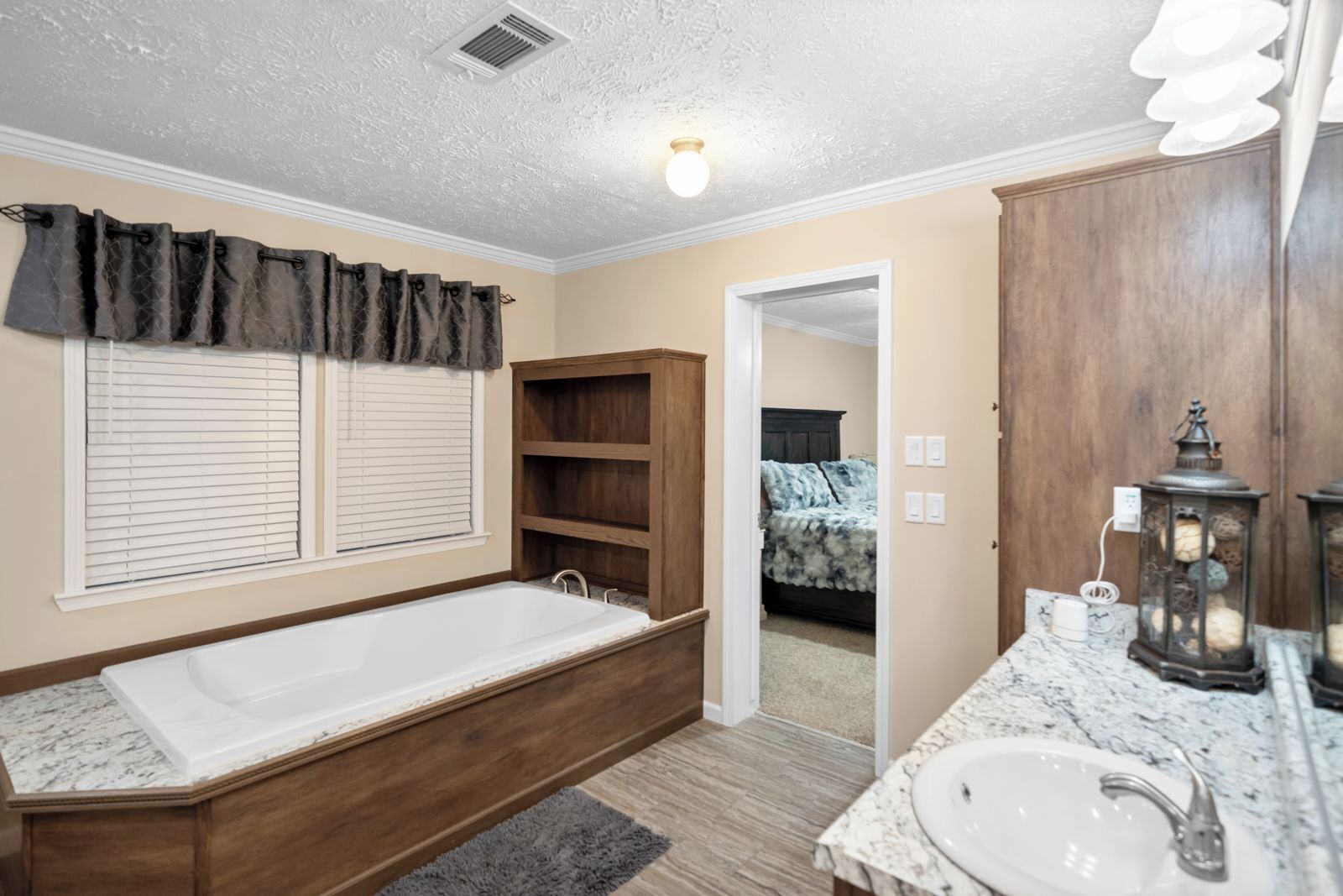 A bathroom with a bathtub, a sink, and a vanity. There is a window with blinds, a door leading to a bedroom, and a ceiling light.