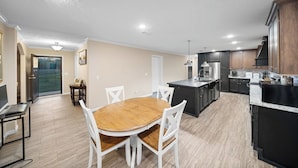 Una cocina moderna con armarios oscuros, una isla central y un comedor con mesa de madera y sillas blancas.