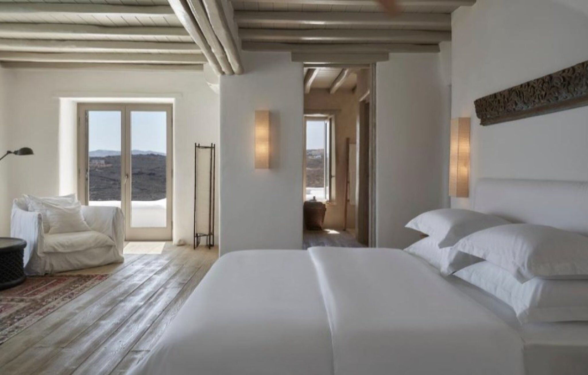 Un dormitorio con una cama grande, una zona de estar con un sillón y vistas a través de una puerta.