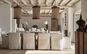A modern hotel room with a dining area featuring a white table and chairs, hanging wicker lamps, and a view of the cityscape through the window. - Villa Lioren, Divine Sea Views, Private Pool, Furnished Terrace, Mykonos (Mykonos)