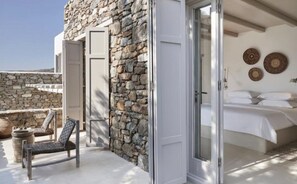 A room with a stone wall, a bed with white linens, and a chair. - Villa Lioren, Divine Sea Views, Private Pool, Furnished Terrace, Mykonos (Mykonos)