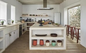 A kitchen with a central island, wooden shelves, and a stone wall. - Villa Lioren, Divine Sea Views, Private Pool, Furnished Terrace, Mykonos (Mykonos)