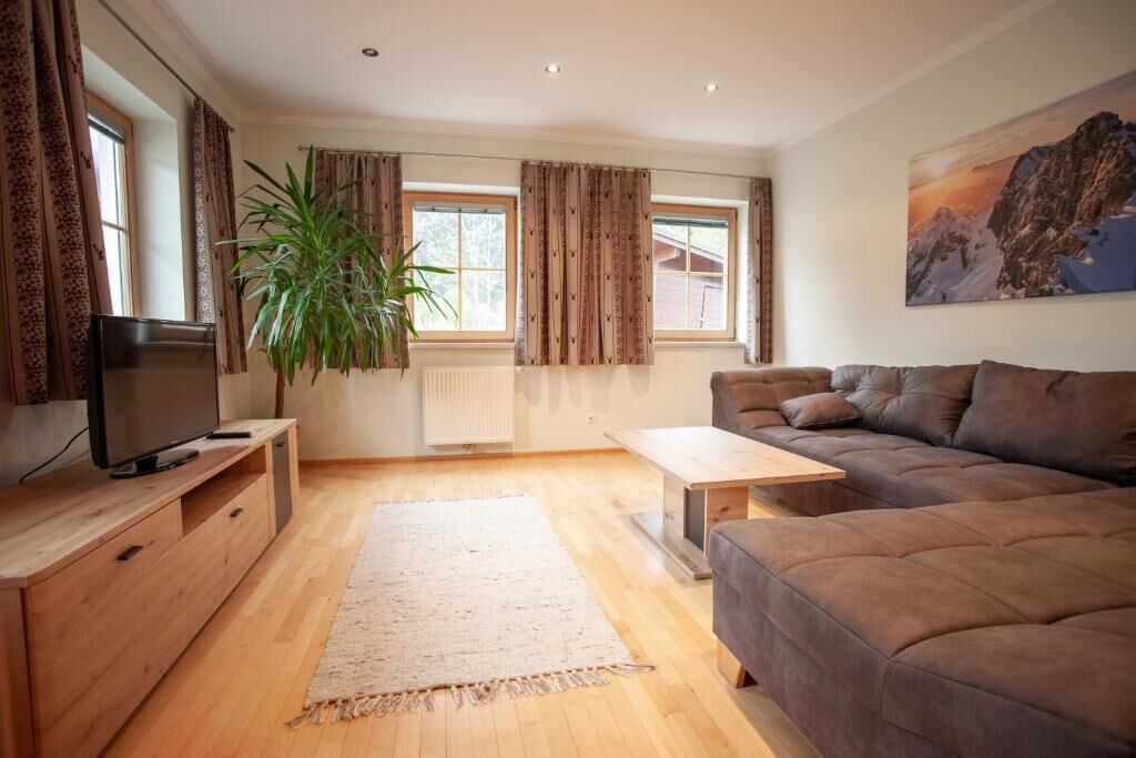 A modern living room with a sofa, TV, wooden cabinet, and a large plant.
