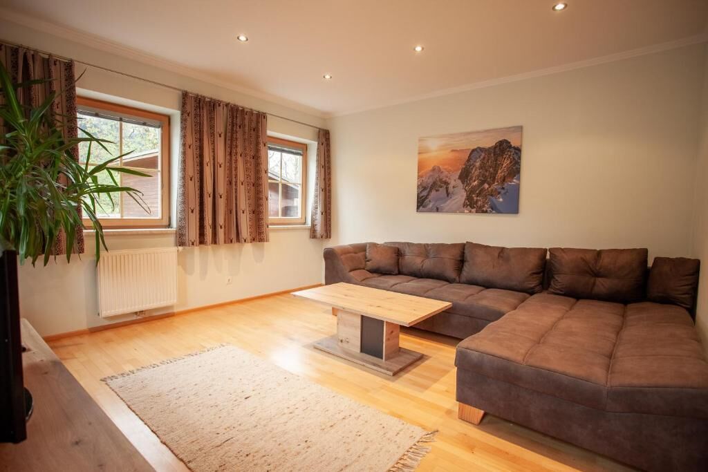 Ein Wohnzimmer mit braunem Sofa, einem Holztisch, einem Fenster mit Vorhängen, einer Heizung und einem Bild an der Wand.