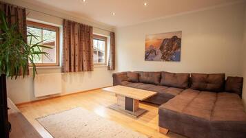 Ein Wohnzimmer mit braunem Sofa, einem Holztisch, einem Fenster mit Vorhängen, einer Heizung und einem Bild an der Wand.