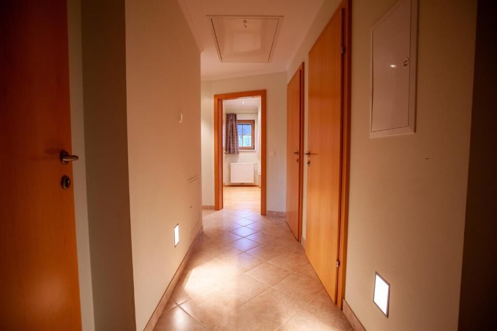Ein Korridor mit Holztüren, Fliesenboden und einer Deckenleuchte.
