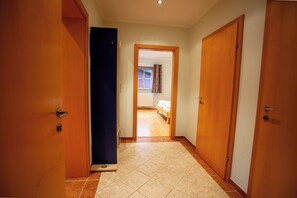 A hallway with wooden doors, a tiled floor, and a bed visible through an open door.