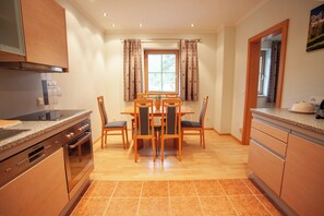 A modern kitchen with a dining area, wooden cabinets, and a window with curtains.