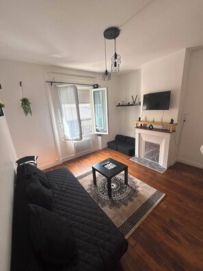 A living room with a black sofa, a coffee table, a fireplace, and a TV mounted on the wall. - Studio on the outskirts of Paris (Saint-Ouen-sur-Seine)