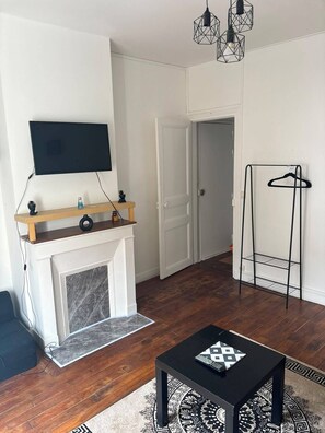 A modern living room with a fireplace, a flat-screen TV mounted on the wall, a wooden coffee table, and a patterned rug. - Studio on the outskirts of Paris (Saint-Ouen-sur-Seine)