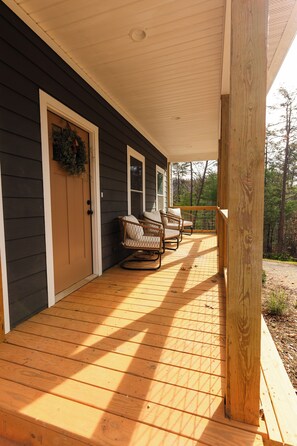 A wooden porch with a covered seating area, a door with a wreath, and a view of trees. - Family and Pet Friendly 3-bedroom house in beautiful Weaverville with Hot Tub (Weaverville)