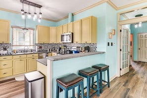 A kitchen with a central island, bar stools, and a microwave. - Walk to Crystal Beach - Family Retreat (Bolivar Peninsula)