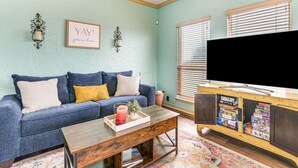 Uma sala de estar com um sofá azul, uma mesa de centro com uma vela e uma televisão sobre um suporte de madeira.