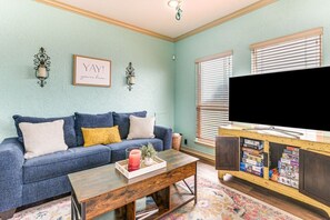 Ein Wohnzimmer mit einem blauen Sofa, einem Couchtisch mit Kerze und einem Fernseher auf einem Holzgestell.