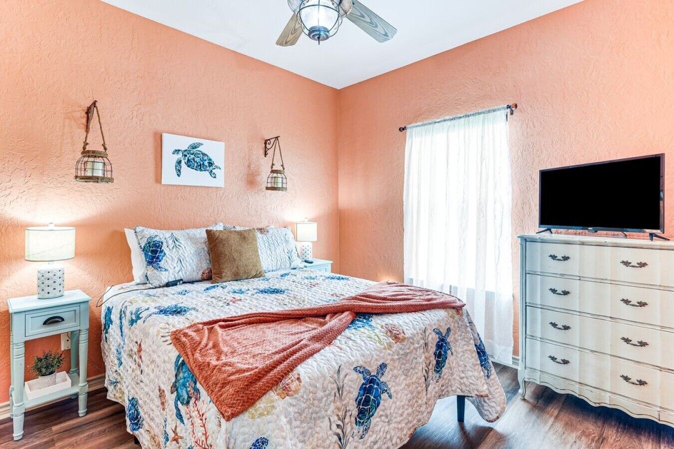 A bedroom with a bed, a dresser, a television, and a window with curtains.