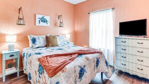 Quarto com cama, penteadeira, televisão e janela com cortinas.