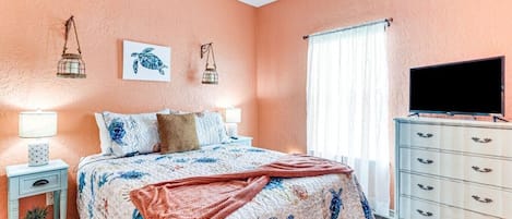 A bedroom with a bed, a dresser, a television, and a window with curtains.