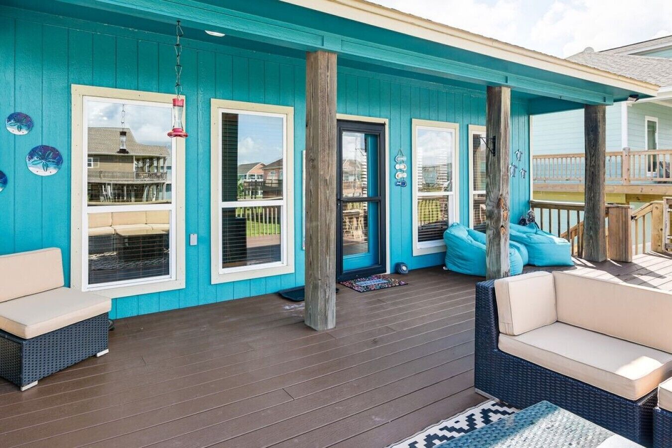 Une véranda couverte, avec une façade bleue, une terrasse en bois et des sièges d’extérieur.
