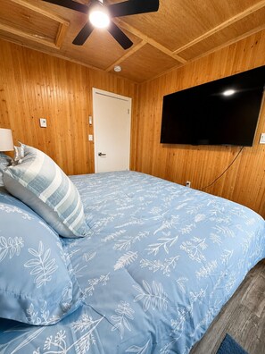 Ein Schlafzimmer mit einem Bett, einem an der Wand befestigten Fernseher und einer Holzbalkendecke.