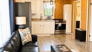 A compact living space with a sofa, a coffee table, a kitchen area with a stove and sink, and wooden walls. - Hydrangeas at Stanley Bridge #4 (Breadalbane)