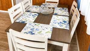 A dining table with floral tablecloths, surrounded by white chairs with woven seat cushions, set against a wooden paneled wall. - Hydrangeas at Stanley Bridge #4 (Breadalbane)