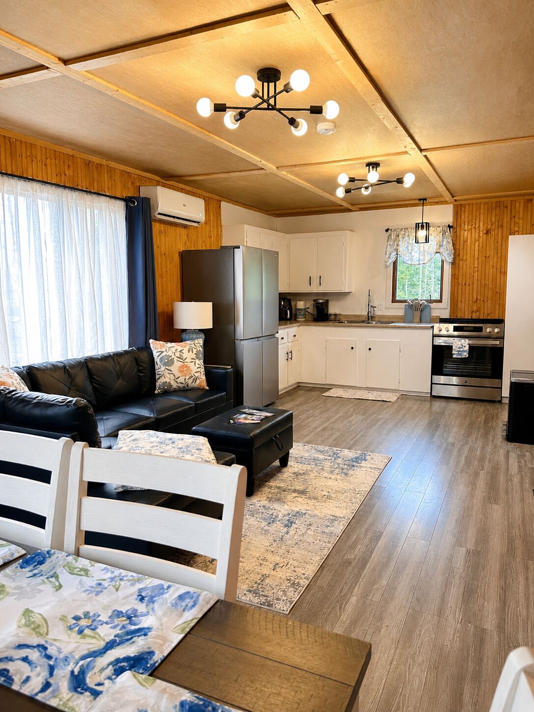 A compact living space with a sofa, dining table, kitchenette, and a ceiling light fixture.