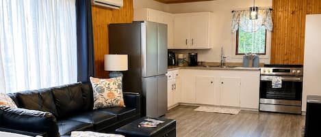 A compact living space with a sofa, dining table, kitchenette, and a ceiling light fixture.