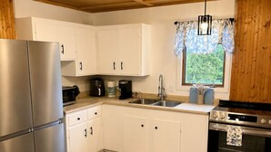 A modern kitchen with white cabinets, stainless steel appliances, a wooden floor, and a window with a view of greenery. - Hydrangeas at Stanley Bridge #4 (Breadalbane)