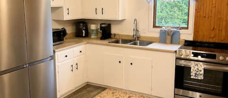 Une cuisine moderne avec des meubles blancs, des appareils en acier inoxydable, un plancher en bois et une fenêtre donnant sur un paysage verdoyant.