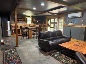 A spacious living area with a leather sofa, wooden dining table, and a kitchen in the background. - Adorable 2-bedroom 1.5 bath cabin in CONECUH National Forest for your getaway (Andalusia)