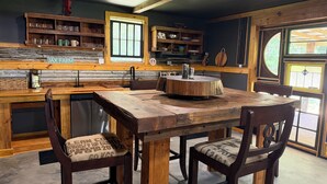 Uma cozinha rústica com uma mesa e cadeiras de madeira, uma janela e uma prateleira com utensílios de cozinha.