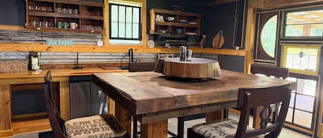 Una cocina rústica con una mesa y sillas de madera, una ventana y un estante con utensilios de cocina.