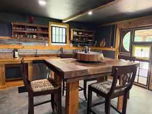 Eine rustikale Küche mit einem Holztisch und Stühlen, einem Fenster und einem Regal mit Küchenutensilien.