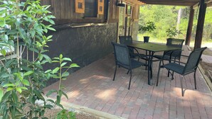 Um pátio ao ar livre com piso de tijolos, pérgola de madeira e uma mesa com cadeiras.