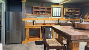 A kitchen with a stainless steel refrigerator, wooden cabinets, and a dining table with benches.