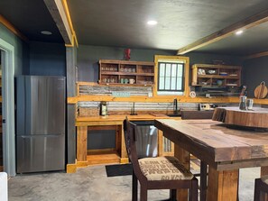 A kitchen with a stainless steel refrigerator, wooden cabinets, and a dining table with benches. - Adorable 2-bedroom cabin in the CONECUH National Forest for your getaway (Andalusia)