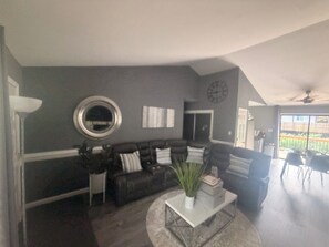 A living room with a dark-colored sofa, a coffee table, and a large mirror on the wall. - Fireside forest retreat Hammocks & Large deck (Charlotte)