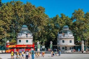 A red double-decker bus with 'City Sightseeing Portugal' written on it, parked in front of a building with two domed structures and flags. - Bright, Renovated 2-Bedroom Apartment Very Close to the Lisbon Zoo (Lisboa)