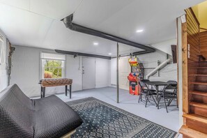 Ein Zimmer mit einer Couch, einem Tisch, einer Spielkonsole und einer Treppe.