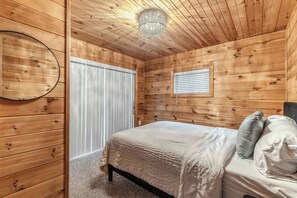 A wooden-paneled room with a bed, a window with blinds, and a circular mirror on the wall. - Cozy Cottage on Turkey Lake/kayaks/Game room! (LaGrange)